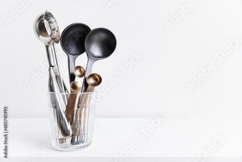 Glass container with copper, stainless steel and black resin spoons on a white background