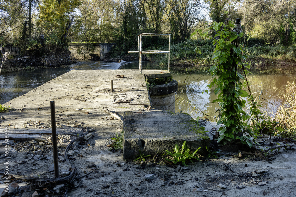 Fototapeta premium a small river dam with its foamy fall and trees on the banks of the river with a cement structure to capture water