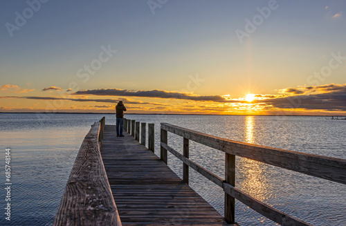 Man Standing At End Of Dock On A Bay At Sunrise Time