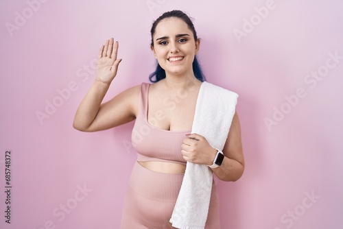Young modern girl with blue hair wearing sportswear over pink background waiving saying hello happy and smiling, friendly welcome gesture