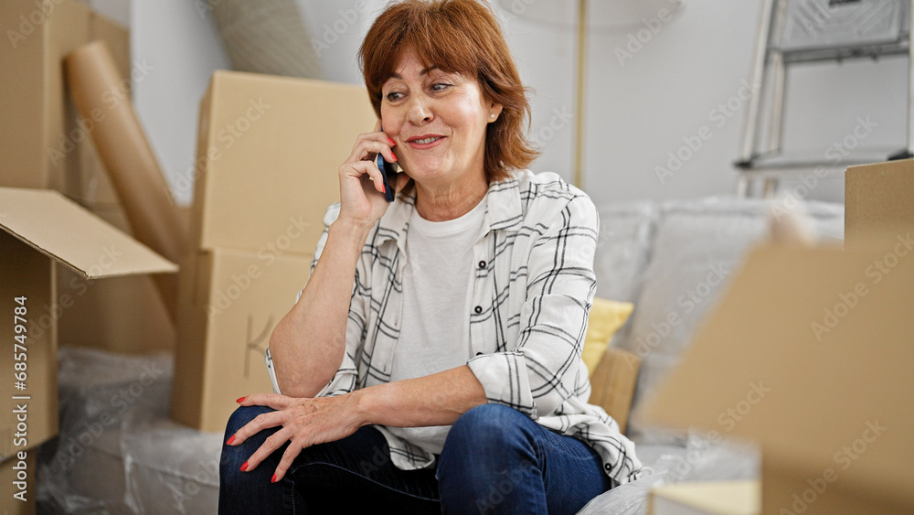 Middle age woman talking on smartphone sitting on sofa at new home Middle age woman talking on smartphone sitting on sofa at new home