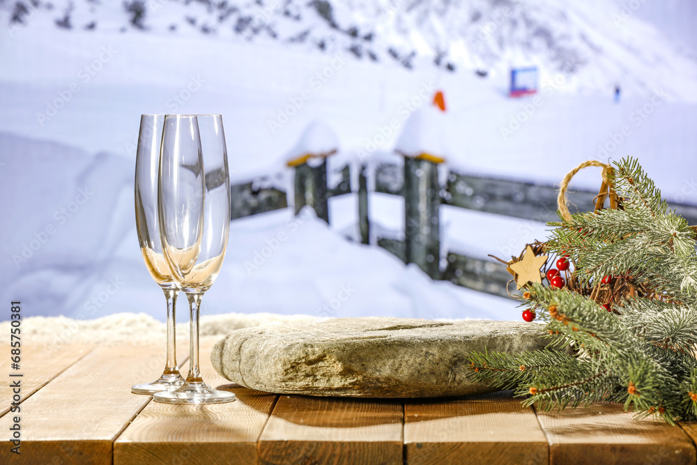 Wooden table with two empty champagne glasses. Empty space for your bottle. Winter landscape of mountains. Mockup background and blue winter sky. Snow and frost decoration. New year time. 