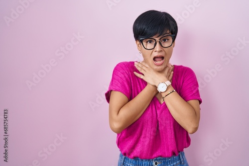 Young asian woman with short hair standing over pink background shouting suffocate because painful strangle. health problem. asphyxiate and suicide concept.