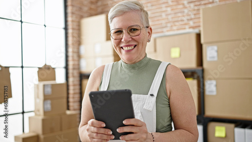 Middle age grey-haired woman ecommerce business worker using touchpad working at office