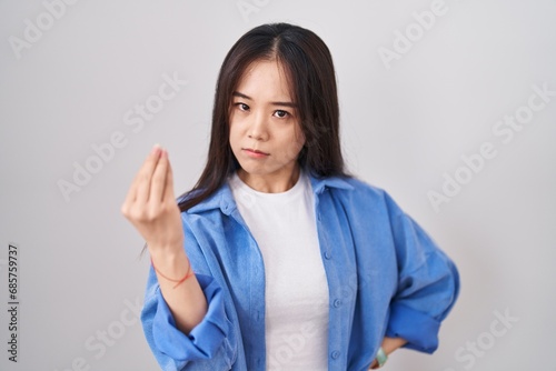 Young chinese woman standing over white background doing italian gesture with hand and fingers confident expression