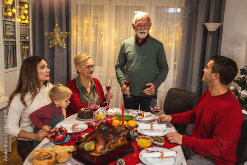 Grandfather is making a toast at the table. Family celebrating Christmas together eating homemade food.