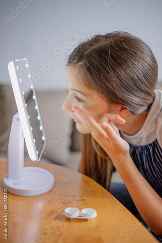 Young woman trying to apply contact lenses in front of mirror. Young girl trying on new contact lenses. Close up of girl trying on beauty medical contact lenses