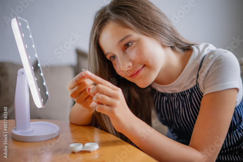 Young woman trying to apply contact lenses in front of mirror. Young girl trying on new contact lenses. Close up of girl trying on beauty medical contact lenses