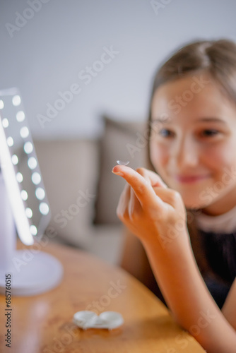 Young woman trying to apply contact lenses in front of mirror. Young girl trying on new contact lenses. Close up of girl trying on beauty medical contact lenses