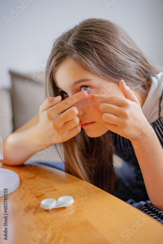 Young woman trying to apply contact lenses in front of mirror. Young girl trying on new contact lenses. Close up of girl trying on beauty medical contact lenses