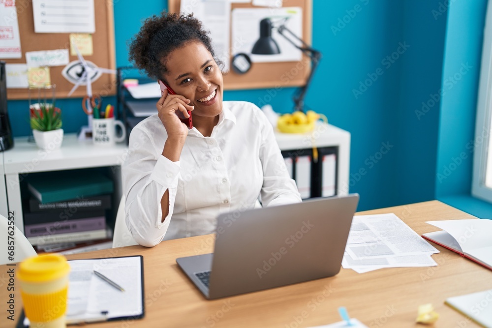 African american woman business worker using laptop talking on smartphone at office