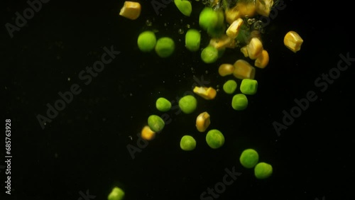 Background video showing a mix of vegetables falling into the water in slow motion. Use of green peas and corn in cooking. High quality 4k footage