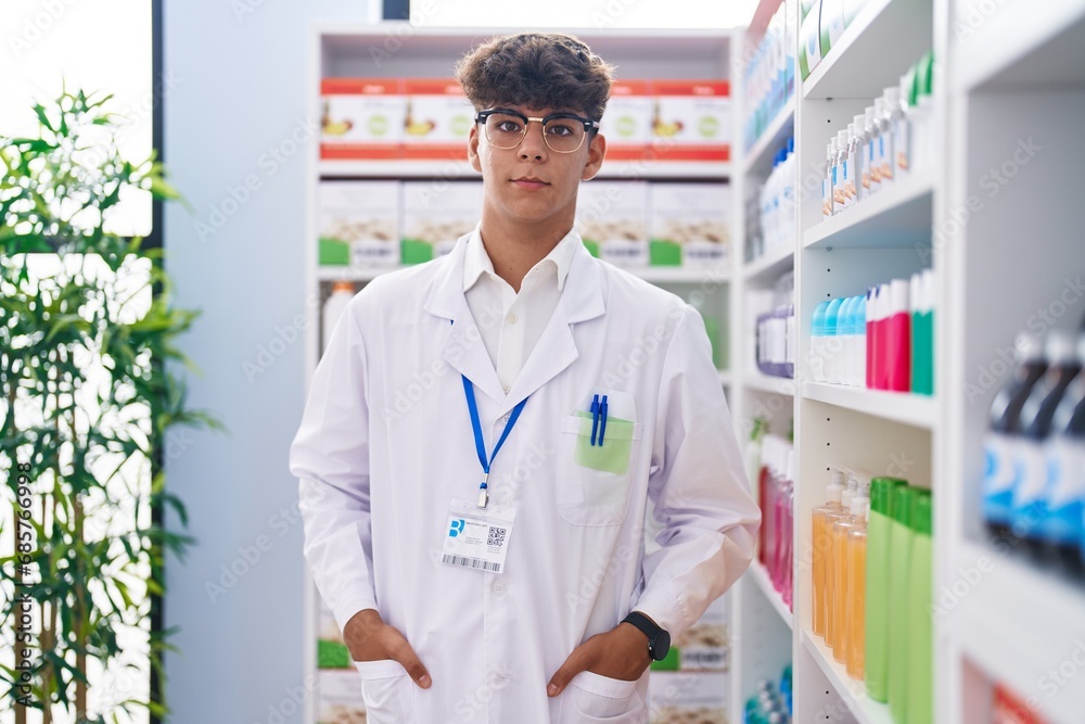 Young hispanic teenager pharmacist standing with relaxed expression at pharmacy Young hispanic teenager pharmacist standing with relaxed expression at pharmacy