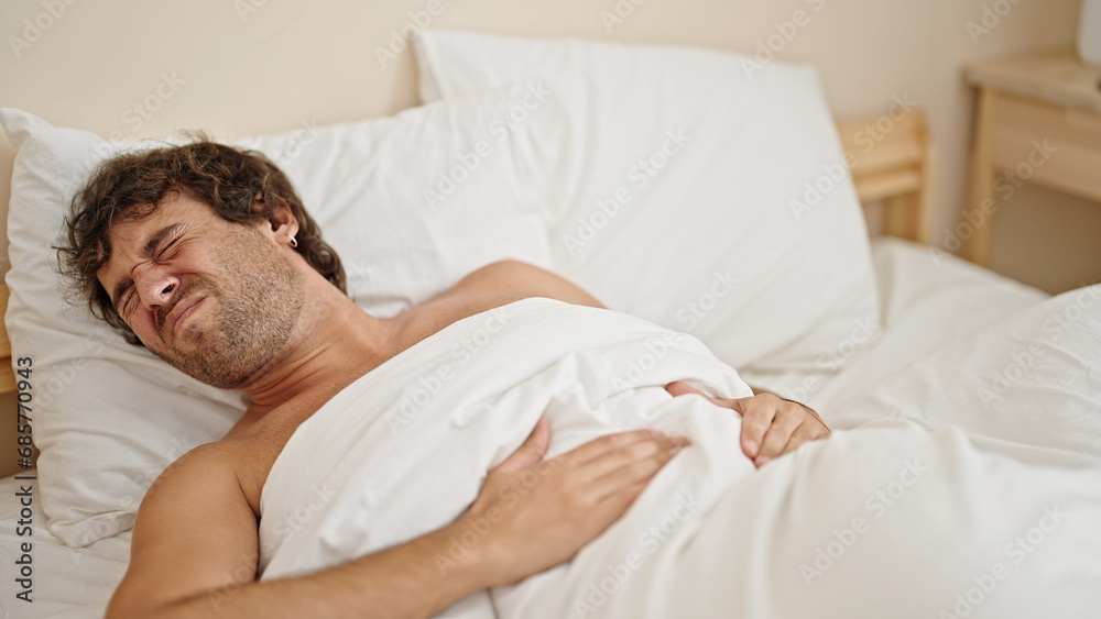 Young hispanic man suffering for stomach ache lying on bed shirtless at bedroom Young hispanic man suffering for stomach ache lying on bed shirtless at bedroom