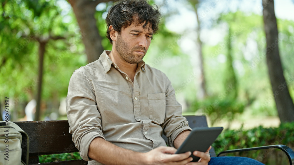 Young hispanic man using touchpad sitting on bench at park Young hispanic man using touchpad sitting on bench at park
