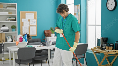 Young hispanic man professional cleaner cleaning floor at office