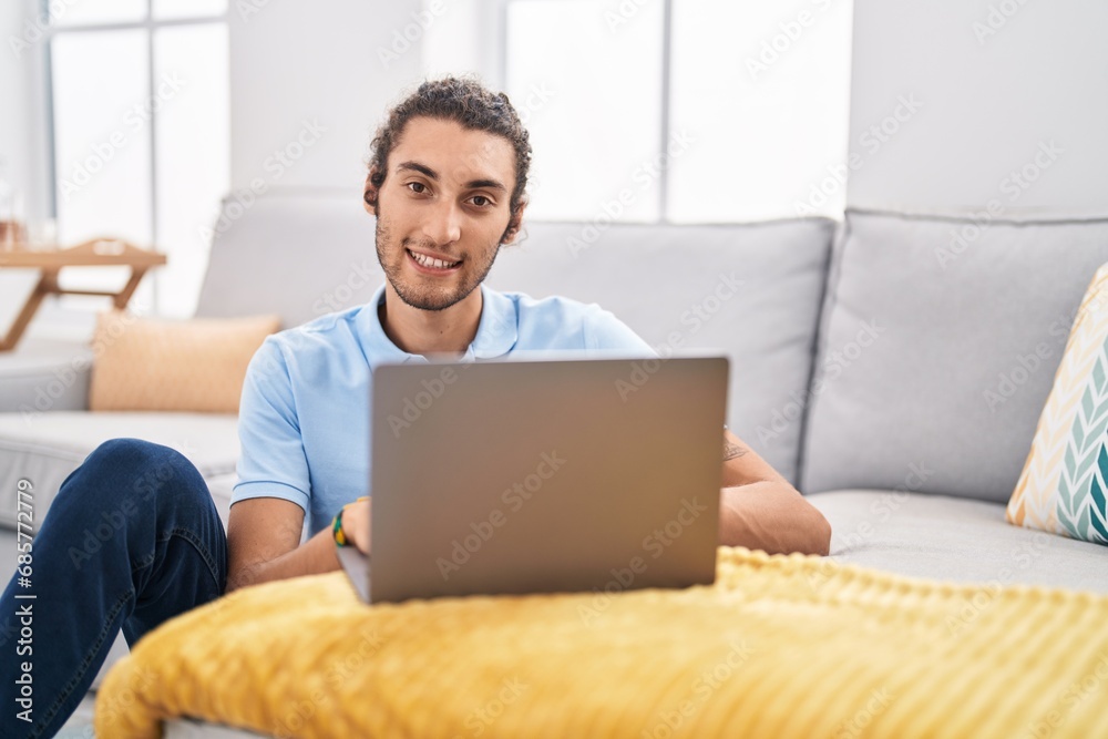 Young hispanic man using laptop sitting on floor at home