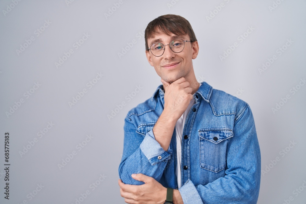 Caucasian blond man standing wearing glasses looking confident at the camera smiling with crossed arms and hand raised on chin. thinking positive. Caucasian blond man standing wearing glasses looking confident at the camera smiling with crossed arms and hand raised on chin. thinking positive.