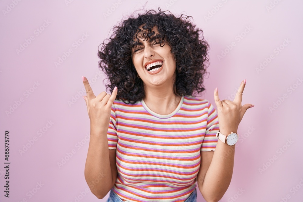 Young middle east woman standing over pink background shouting with crazy expression doing rock symbol with hands up. music star. heavy music concept. Young middle east woman standing over pink background shouting with crazy expression doing rock symbol with hands up. music star. heavy music concept.