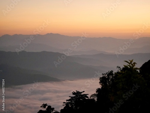 The mist flows through the mountain forest  Sun shining into tropical forest  Mist drifts through mountain ridges in the morning  slow floating fog blowing cover on the top of mountain 