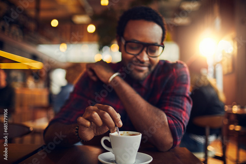 Young man sitting in cafe stirring or mixing a coffee mug photo