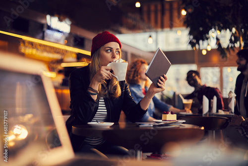 Young woman drinking big coffee cup and using tablet in cafe photo