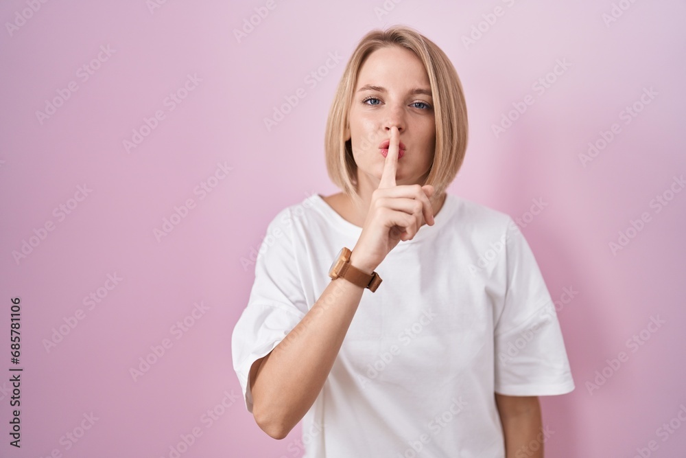 Young caucasian woman standing over pink background asking to be quiet with finger on lips. silence and secret concept. - obrazy, fototapety, plakaty 