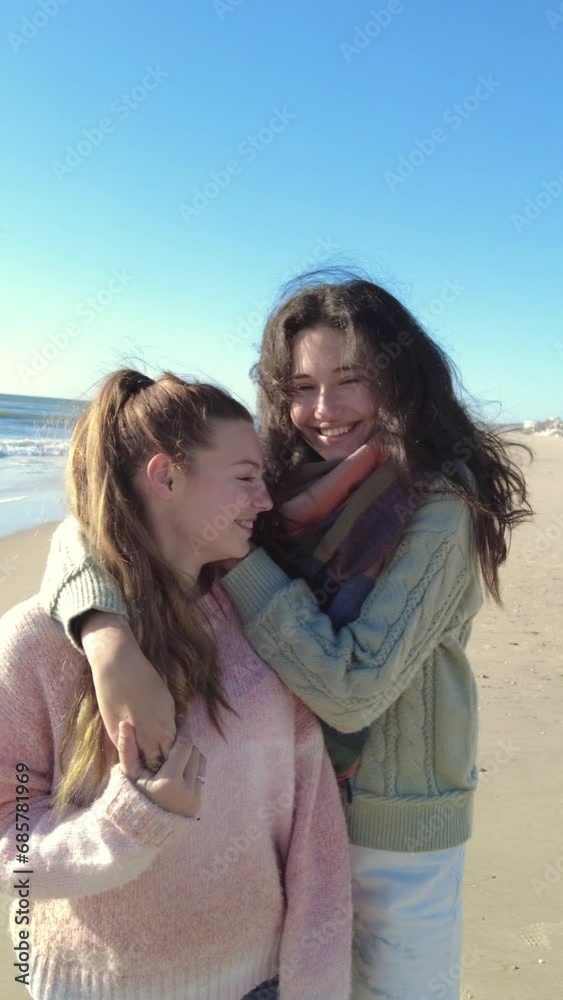 Loving young lesbian couple in warm clothes with dark hair embracing and looking at each other at beach Loving young lesbian couple in warm clothes with dark hair embracing and looking at each other at beach