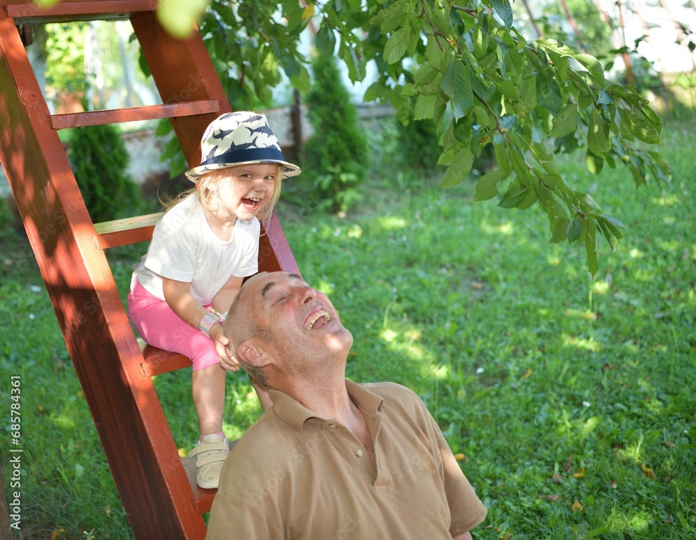 Little girl licking sweet lollipop and grandfather playing and laughing on the wooden stairs