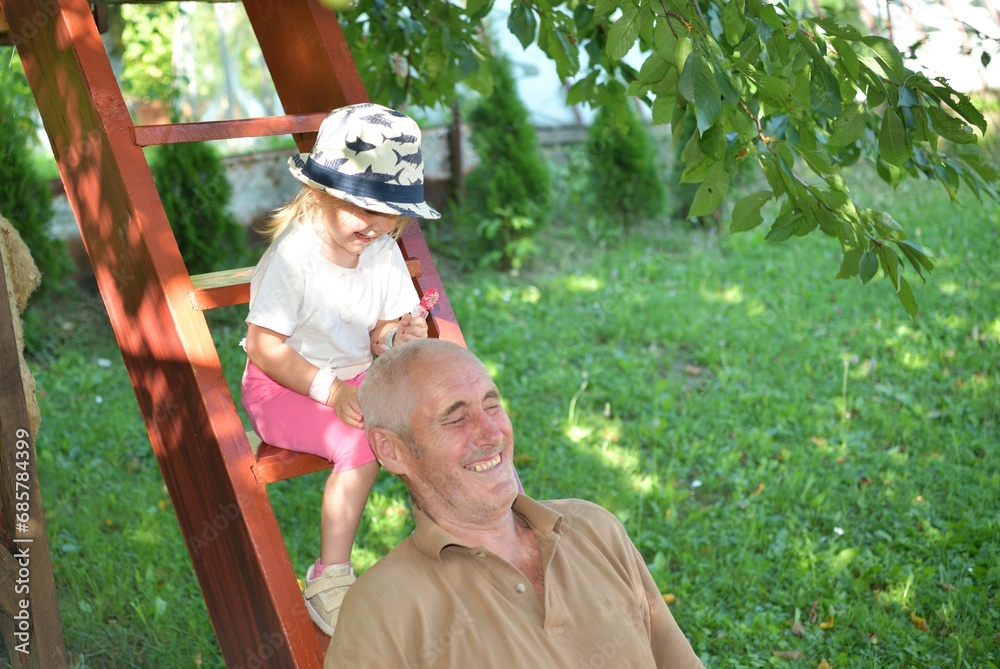 Little girl licking sweet lollipop and grandfather playing and laughing on the wooden stairs