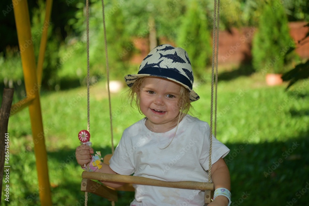 A girl licking with a tongue sweet scrapper lollipop while swinging on a tree