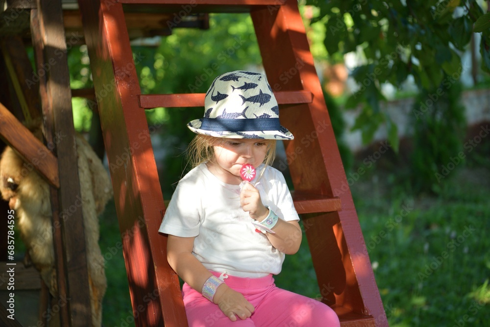 A girl licking with a tongue sweet scrapper lollipop while swinging on a tree