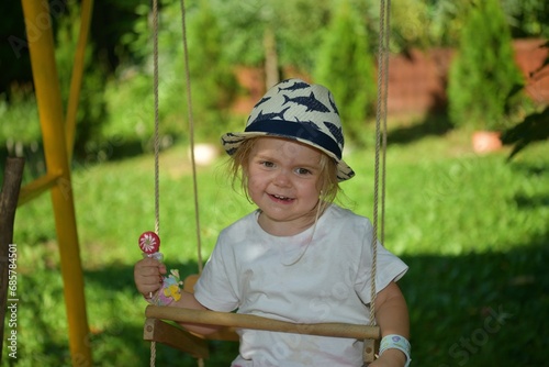 Obraz na płótnie A girl licking with a tongue sweet scrapper lollipop while swinging on a tree w salonie