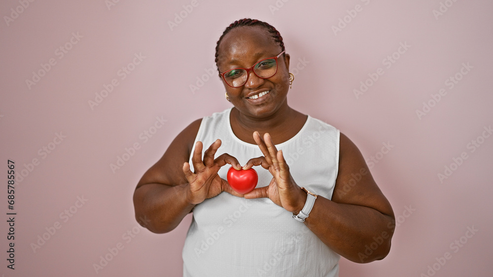 Confident african american woman joyfully holds heart shape with hands, smiling over isolated pink wall background, expressing positive lifestyle Confident african american woman joyfully holds heart shape with hands, smiling over isolated pink wall background, expressing positive lifestyle
