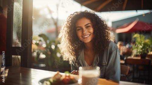Young woman smiling while sitting outside at a table on a restaurant patio and eating delicious. Street food concept. © Oulaphone
