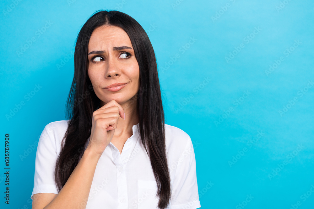 Photo of doubtful unsure girl dressed white shirt arm hand chin looking empty space isolated blue color background Photo of doubtful unsure girl dressed white shirt arm hand chin looking empty space isolated blue color background