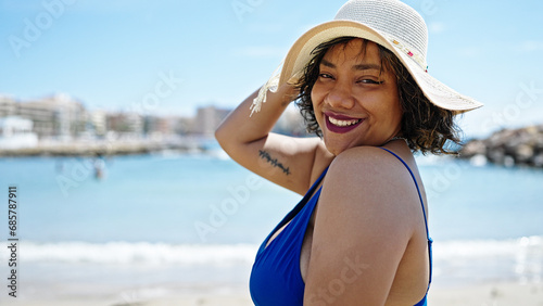 Young beautiful latin woman tourist smiling confident wearing swimsuit and summer hat at beach