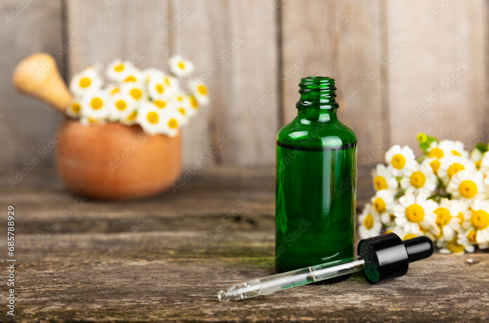 Glass bottle with chamomile essential oil on an old wooden background. Chamomile flowers, close up. Aromatherapy, spa and herbal medicine ingredients. Beauty concept.Copy space. Natural cosmetic