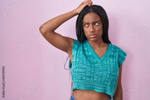 Young african american with braids standing over pink background confuse and wondering about question. uncertain with doubt, thinking with hand on head. pensive concept.