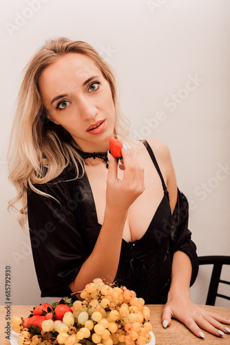 Woman eating strawberries. Sexy blonde woman in kitchen eating berries