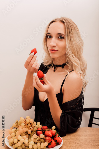 Woman eating strawberries. Sexy blonde woman in kitchen eating berries