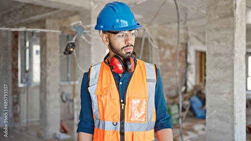 Young hispanic man builder wearing hardhat at construction site
