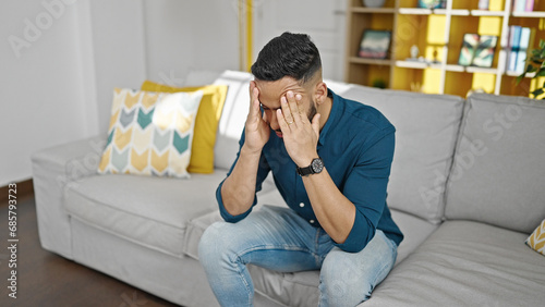 Young hispanic man stressed sitting on sofa at home