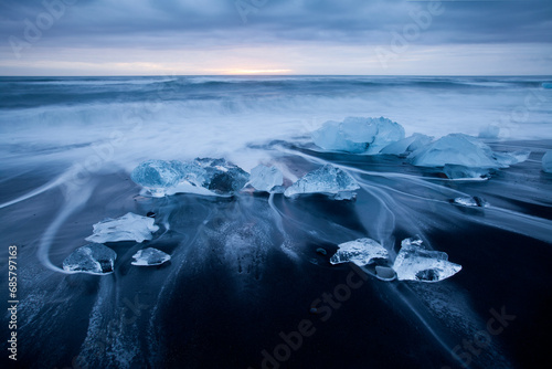 Long exposure of ocean waves and glacial ice chunks on a black sand beach near Jokulsarlon Glacier Lagoon in southeastern Iceland 