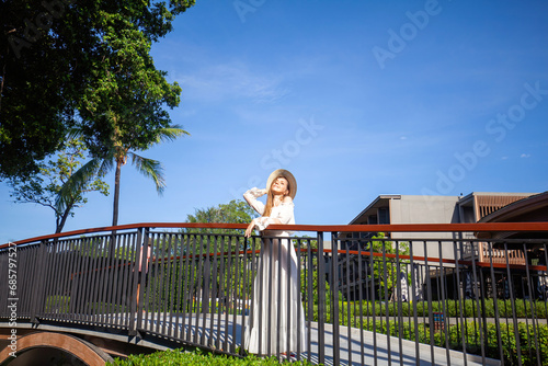 Elegance and style. Woman on resort bridge against blue sky, palm tree, and resort architecture. Summer travel.