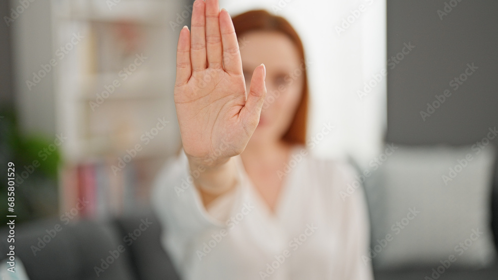 Young redhead woman doing stop gesture with hand at home