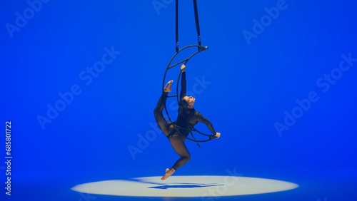 Rhythmic gymnastics girl performs the scum on one arm in the air on a metal rotating structure moon. Blue background