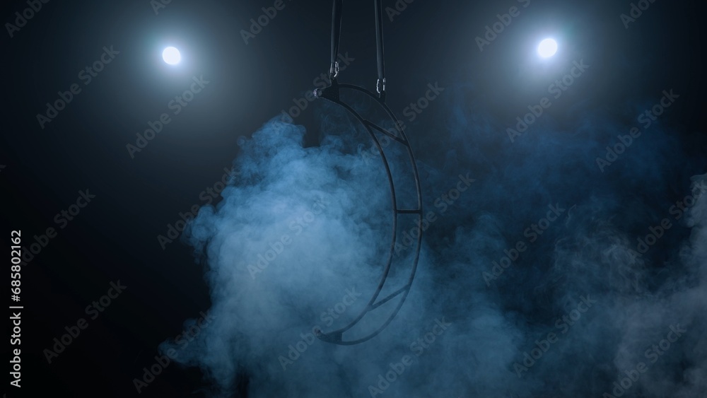 Aerial gymnastics apparatus in the shape of the moon. Black background with blue smoke