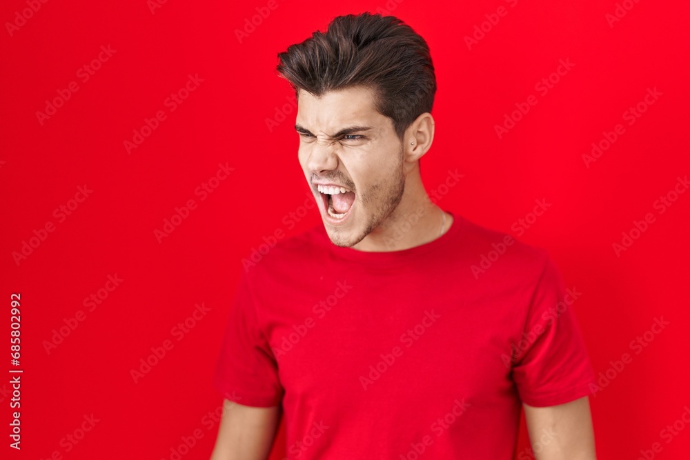 Young hispanic man standing over red background angry and mad screaming frustrated and furious, shouting with anger. rage and aggressive concept. Young hispanic man standing over red background angry and mad screaming frustrated and furious, shouting with anger. rage and aggressive concept.