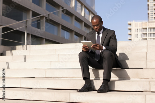 African businessman sitting on steps with digital tablet, outdoor near office building photo